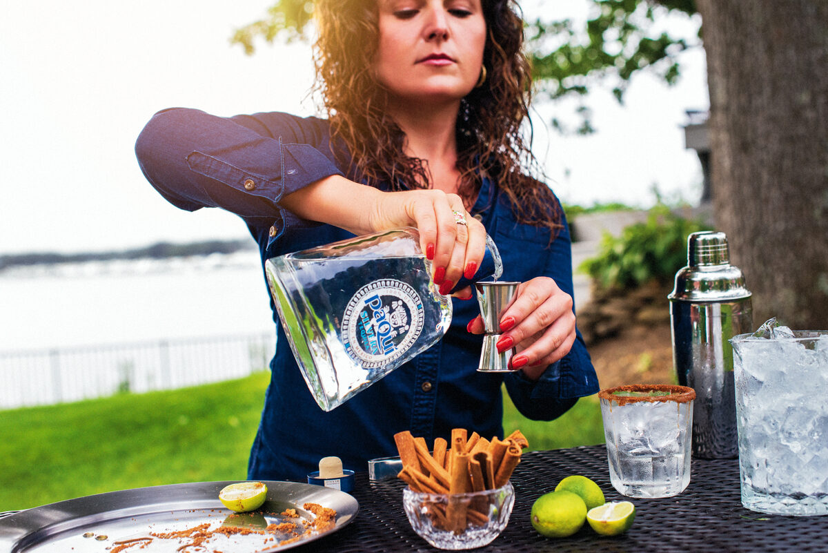 Woman measuring PaQui Tequila with jigger at waterfront bar