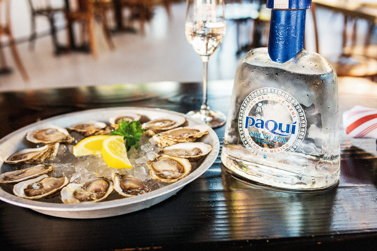 PaQui Silvera Tequila bottle with star anise cocktail, deep blue reflective surface